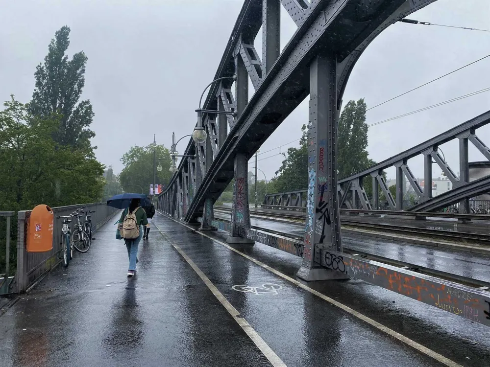 Eine Person mit Regenschirm läuft über eine Brücke. Sie entfernt sich vom Betrachter.