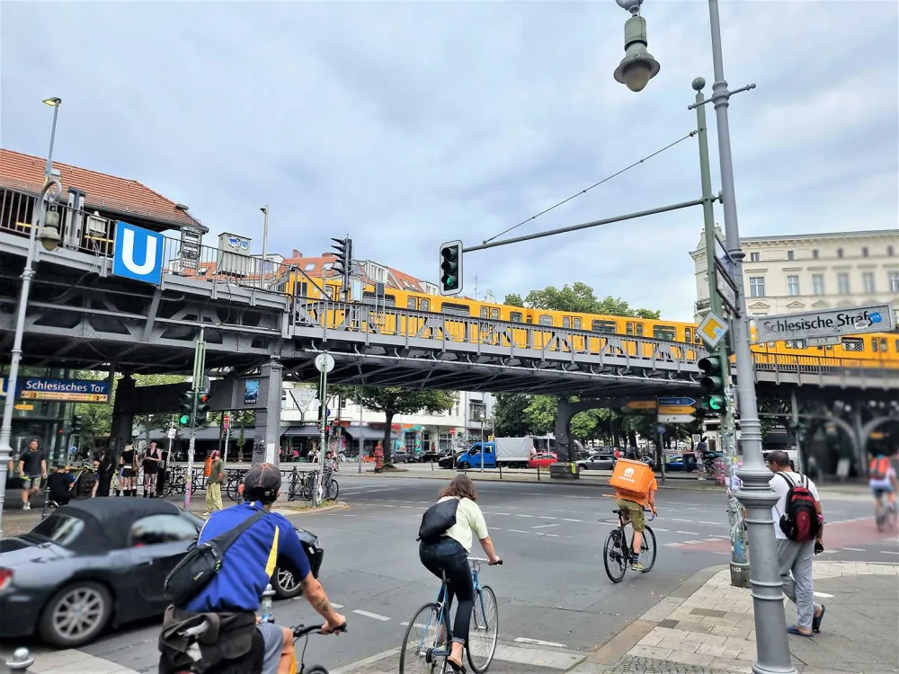 Straßenszene am Schlesischem Tor in Kreuzberg: Fahrradfahrer, ein Auto, eine gelbe Hochbahn und der U-Bahnhof.
