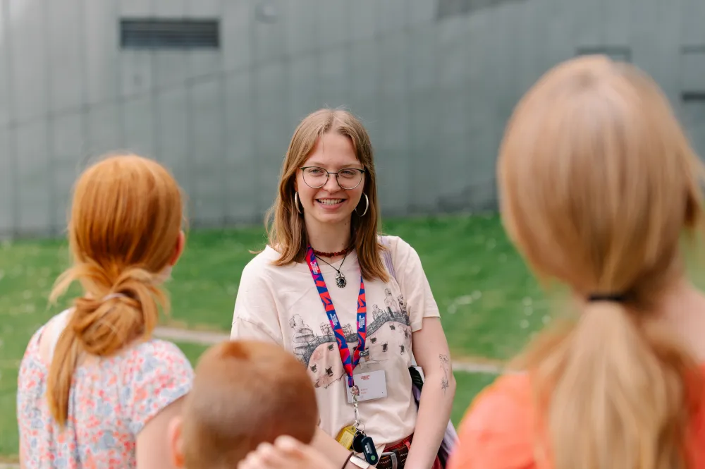 Visitors are standing with a young woman in a meadow in front of a steel building