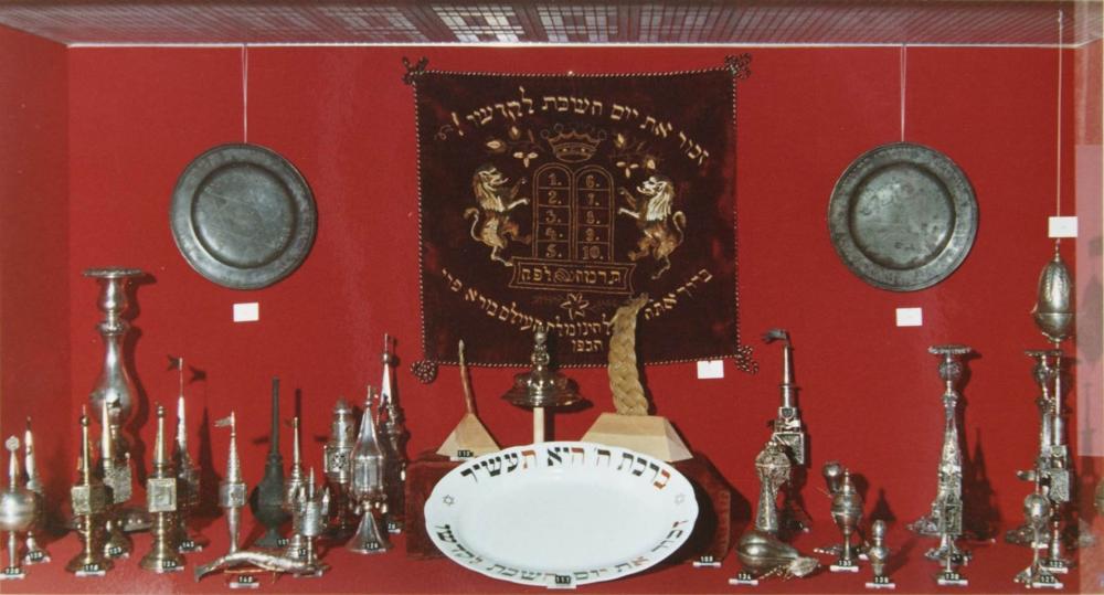 Foto einer Ausstellungsvitrine mit Judaica-Objekten vor rotem Hintergrund