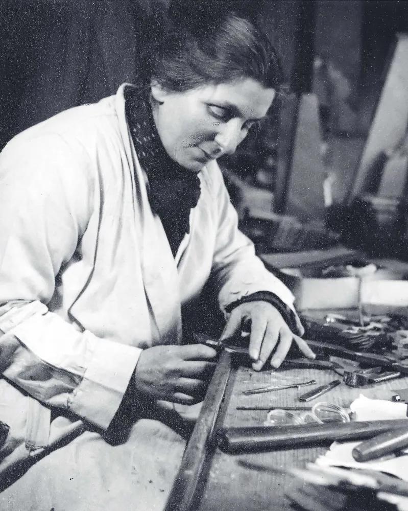Historische Aufnahme einer vornübergebeugt an einem Werktisch arbeitende Frau. 