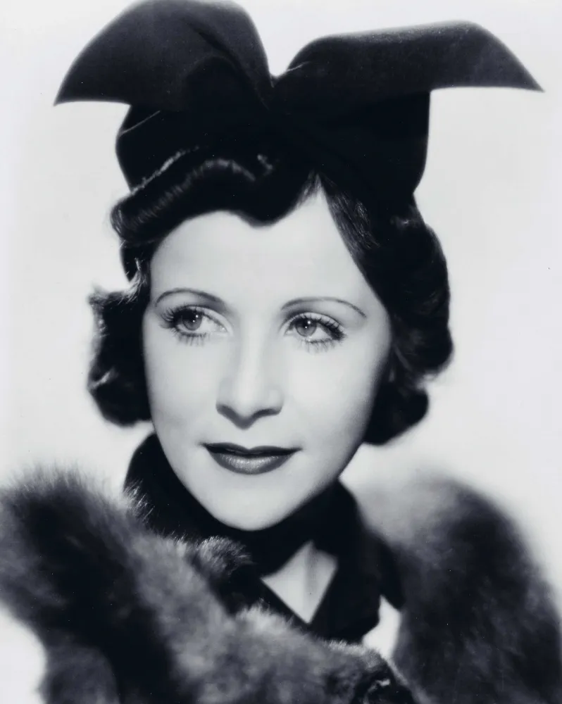  Black and white photograph of a woman wearing an extravagant black hat and a fur-trimmed top.