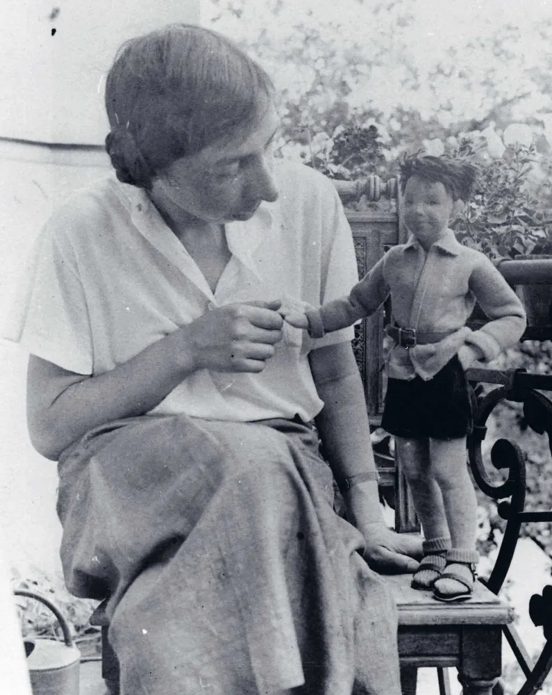 Schwarz-weiß-Foto einer Frau neben der rechts eine Puppe steht, deren Hand sie hält und die sie anblickt.