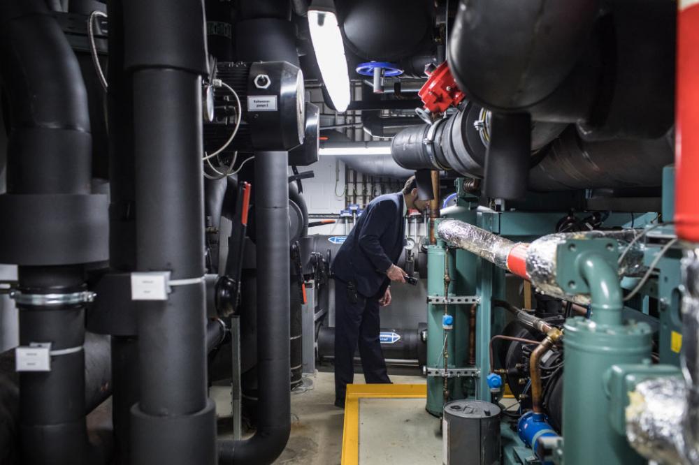 A security guard checking a room full of pipes and cables.