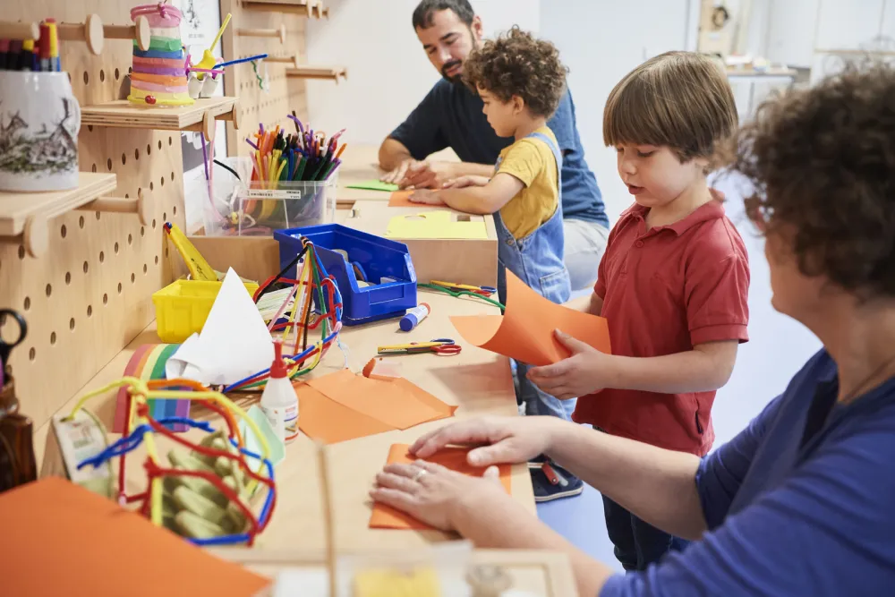 Two children and two adults tinkering with paper at a workbench.