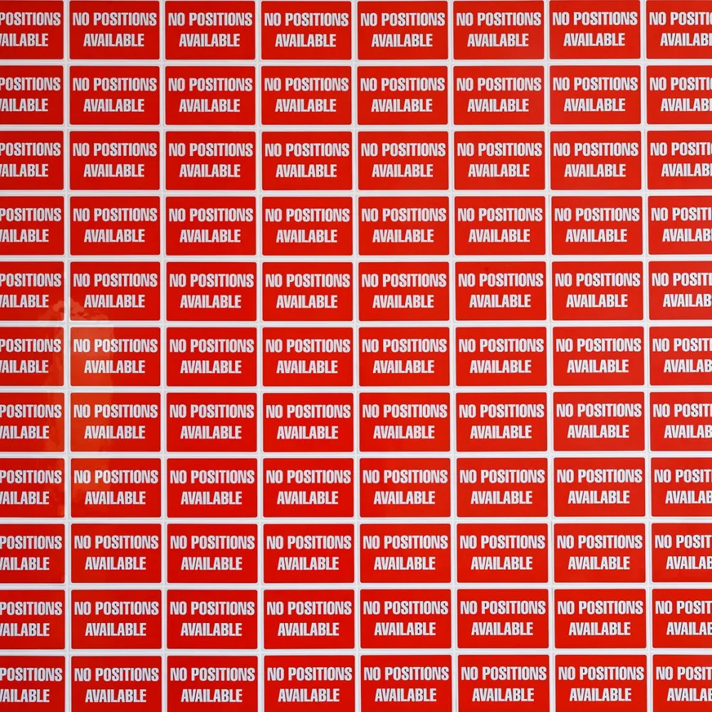 Eine Wand tapeziert mit rechteckigen, roten Schildern, auf denen steht: „NO POSITIONS AVAILABLE“.