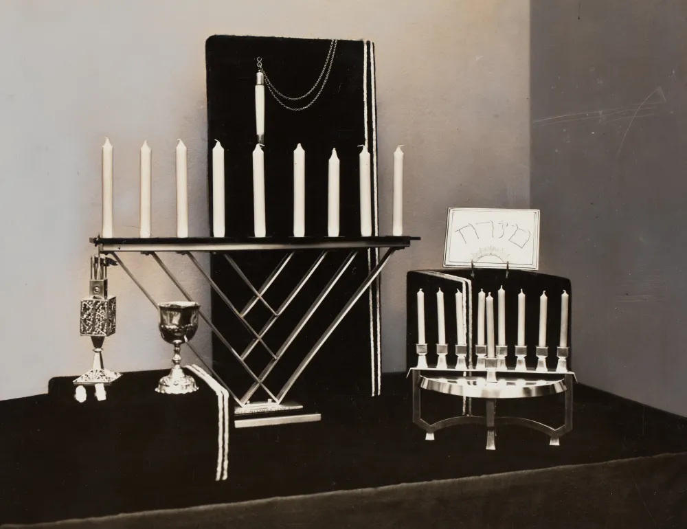 Das Bild zeigt mittig eine Chanukkah-Lampe mit neun Kerzen, rechts und links davon weitere silberne Judaica.