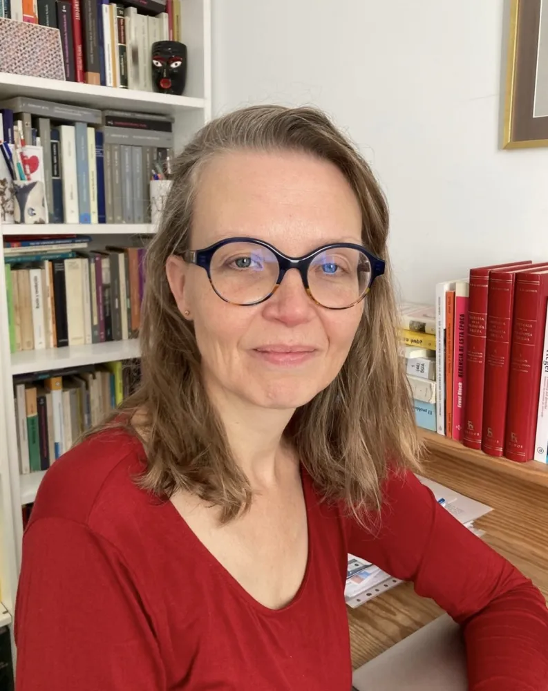 A woman wearing glasses looks friendly at the camera.