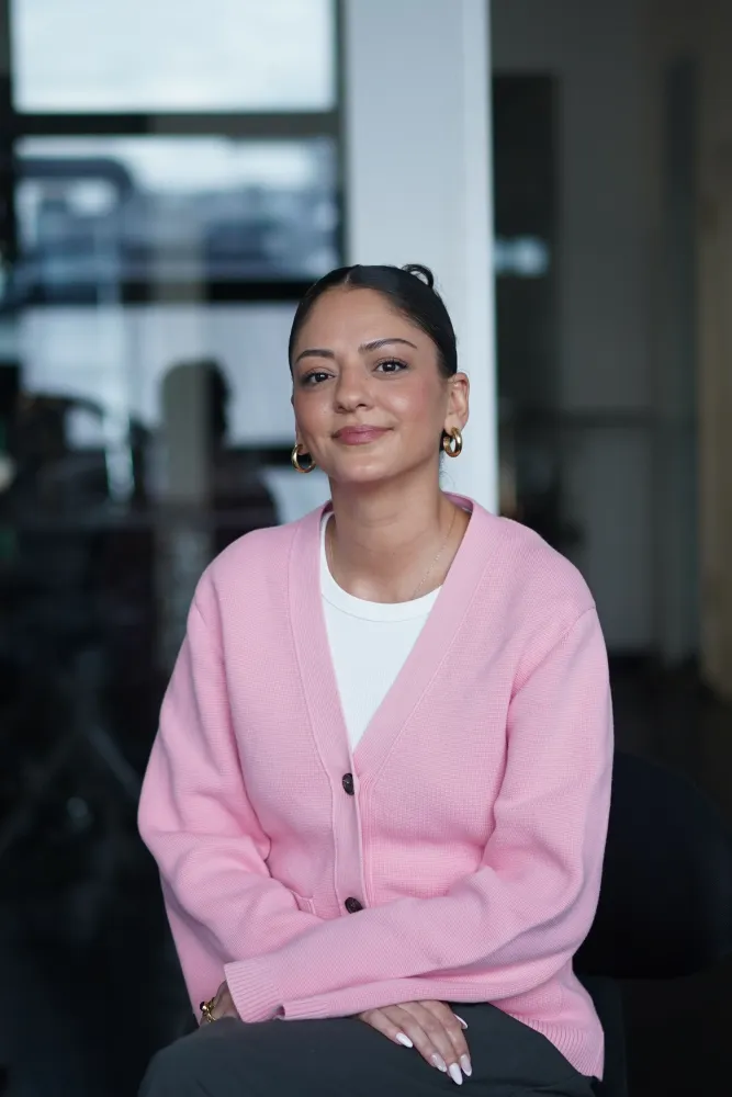 Portrait Foto einer jungen Frau vor unscharfem Hintergrund. Sie tr&auml;gt ein wei&szlig;es Tshirt und dar&uuml;ber eine rosa Strickjacke.