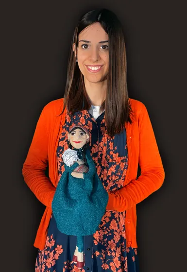 A woman with long, brown hair is holding a puppet in her hands.