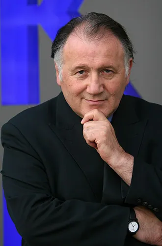 Portr&auml;t eines Mannes, der die Hand ans Kinn h&auml;lt und mit fragendem L&auml;cheln in die Kamera schaut.