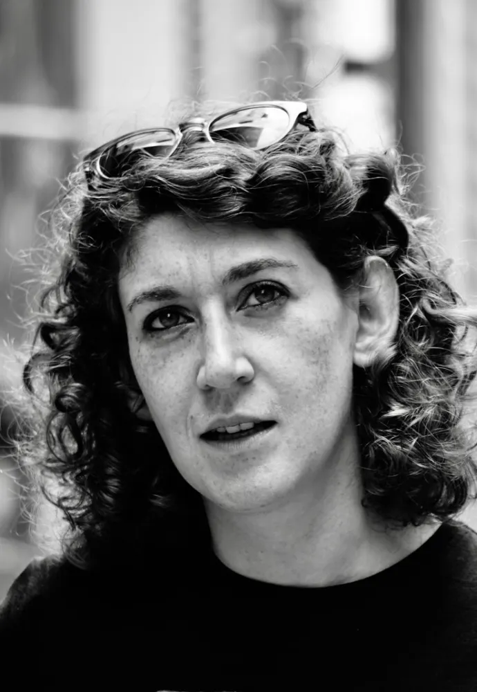 Schwarz-weiß-Porträt einer Frau mit halblangen Locken und Brille im Haar, die nach schräg oben schaut.