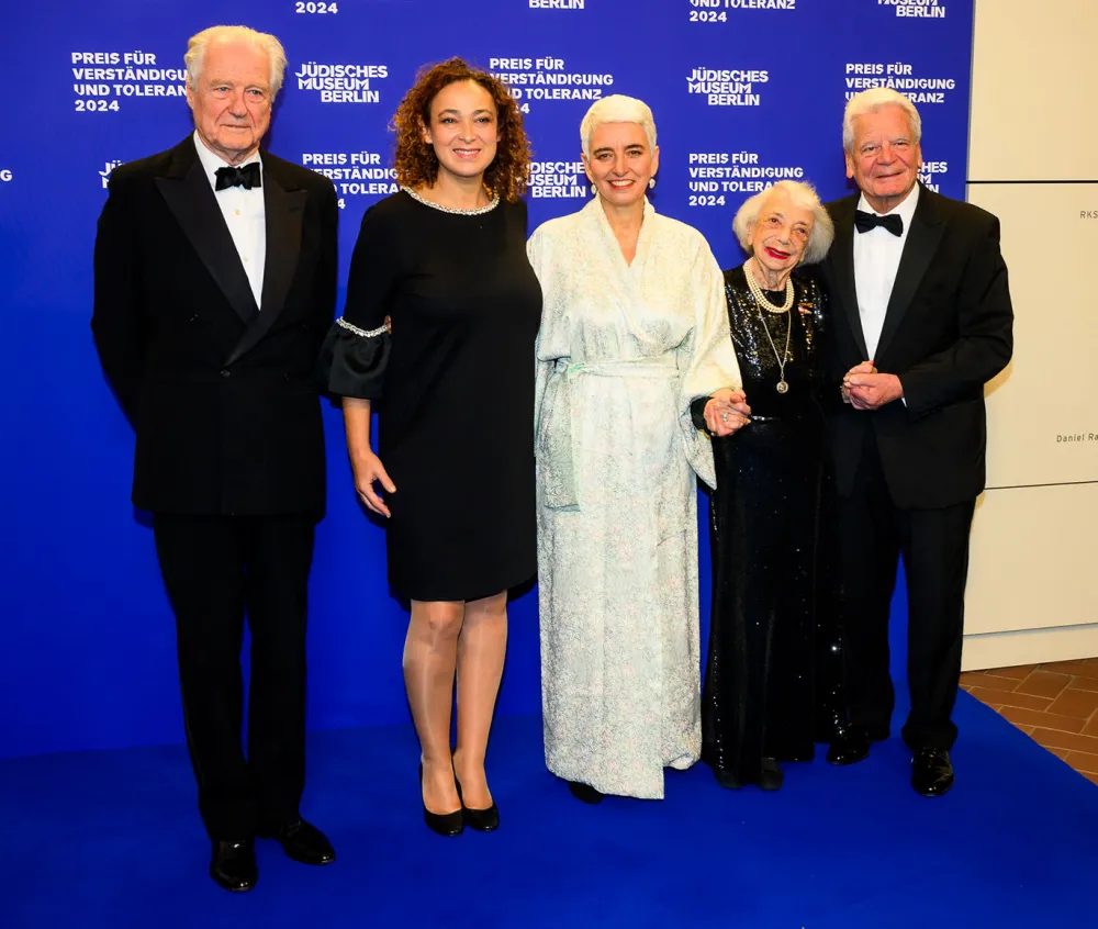 Five people stand on a blue carpet as a group smiling.