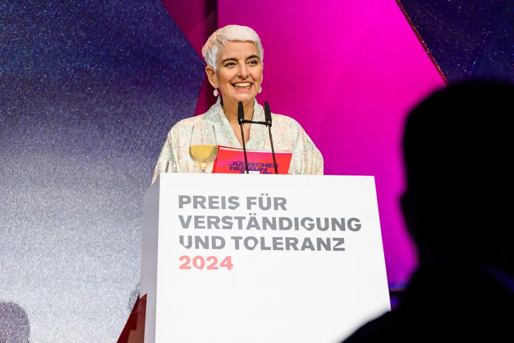 A woman stands at a podium desk and delivers a speech.