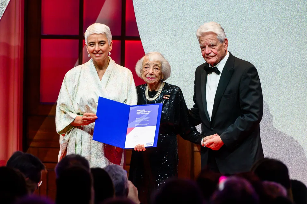 Three people stand next to each other, the one in the middle holding an award certificate.