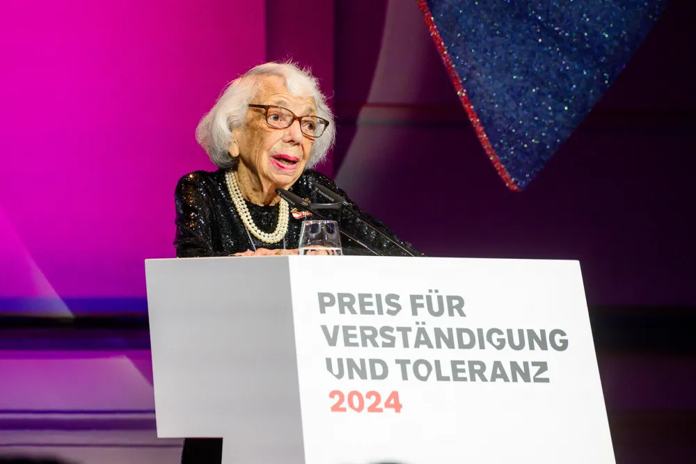 A woman stands at a podium desk and delivers a speech.