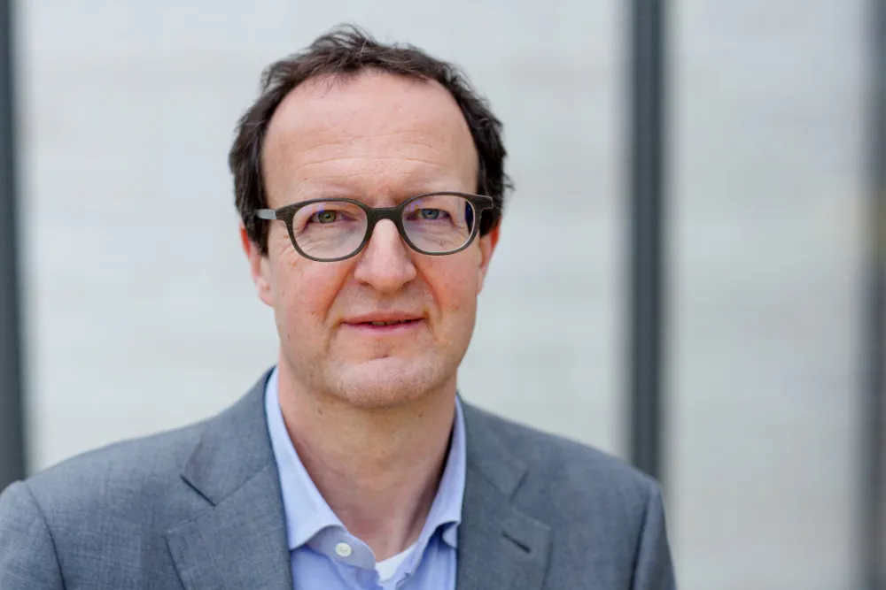 Mann mit Brille schaut freundlich in die Kamera und hat einen Anzug an.