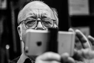 Schwarz-Wei&szlig;-Foto eines Mannes mit Glatze und Brille, der ein iPhone auf einem Stativ festh&auml;lt und damit filmt.