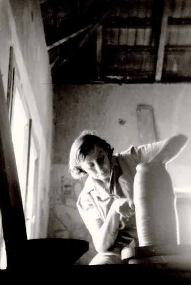 Schwarz-weiß-Fotografie einer Frau, die an einer Drehscheibe an einer töpferner Vase arbeitet.