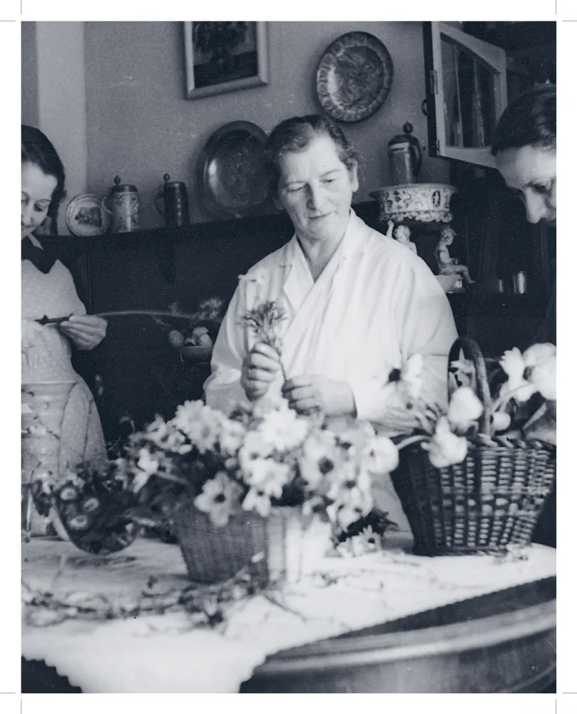 Sepiafarbene Aufnahme, die drei Frauen zeigt, die Blumengestecke in Weidenkörben zusammenstellen.
