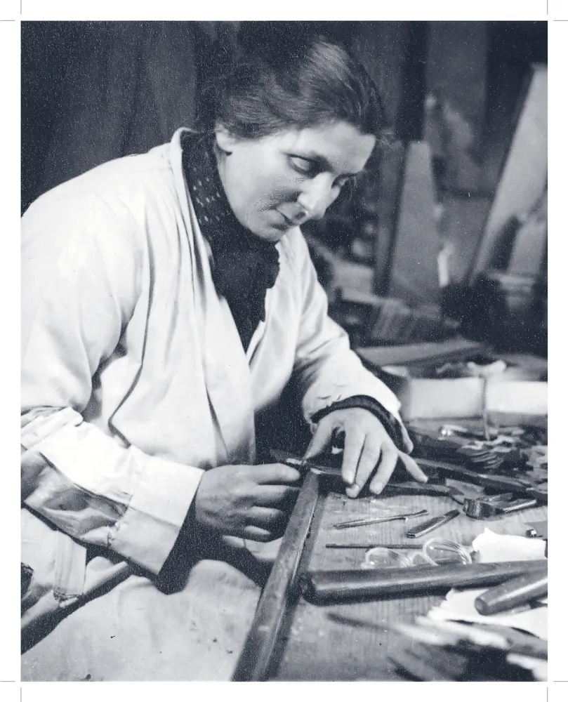 Historische Aufnahme einer vornübergebeugt an einem Werktisch arbeitende Frau. 