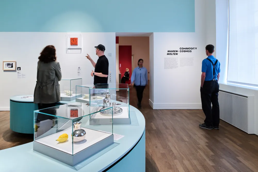 Ausstellungsansicht mit vier Personen und Objekten, die in Vitrinen liegen.