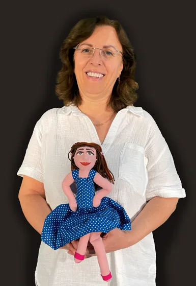 A woman with chin-long, brown hair, wearing a white blouse, is holding a doll in her hands.