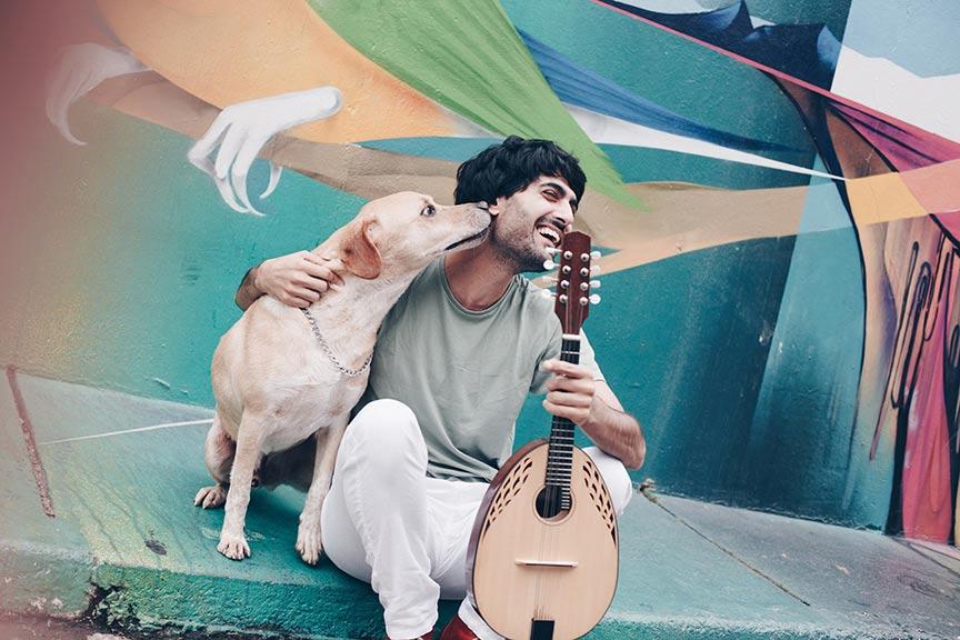 Laughing man with dog and mandolin sits in front of colorful painted wall