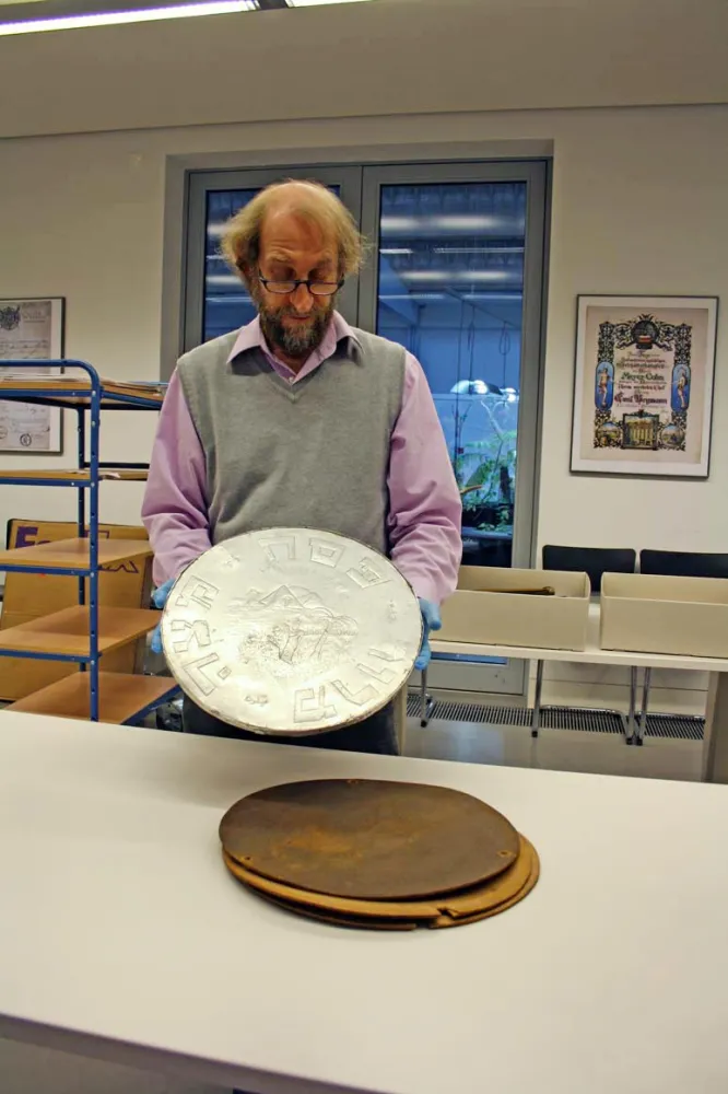 A man holds a metal disk up to the camera.
