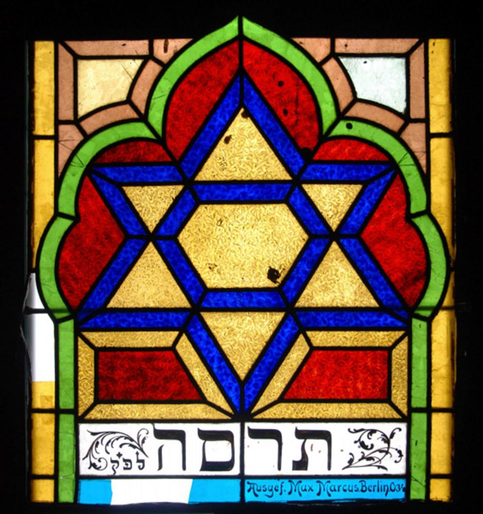 Colorfult stained glass window depicting the star of david with Hebrew text at the bottom