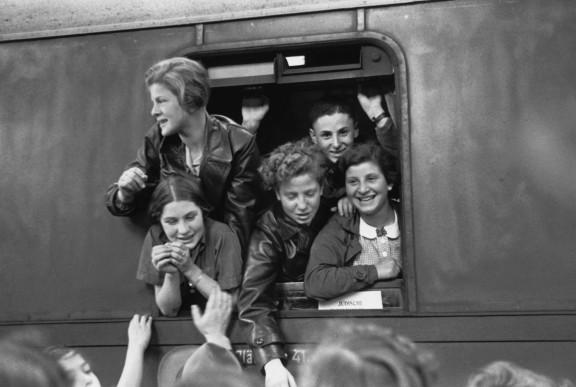 Black and white photography of teenage girls and boys joyfully leaning out of the window of a train