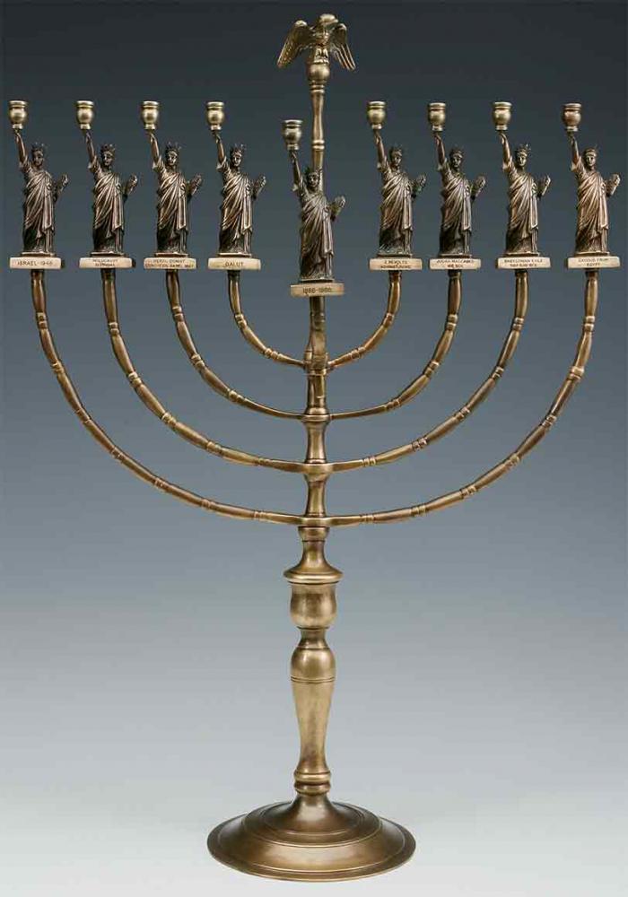 Candelabrum with a round base fitted to a central stem from which eight branches extend, four on either side, each of them topped with a miniature Statue of Liberty