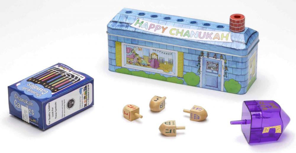 Multi-piece children’s set for Hanukkah consisting of dreidels, candles, and a menorah in the form of a metal box decorated to resemble a house. The roof features eight depressions to hold the candles; the chimney serves as the shamash.