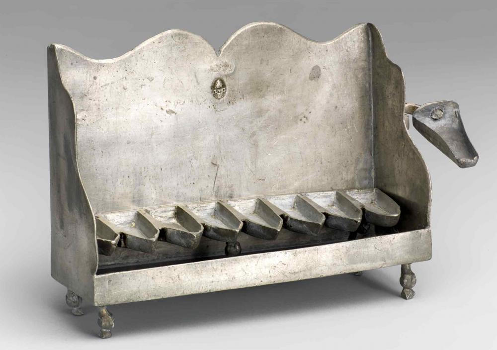  A tin candelabrum in the shape of a bench fitted with eight oil cups, resting on four feet