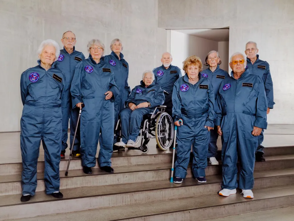 Gruppenbild von zehn &auml;lteren Menschen in Astronautenanz&uuml;gen, eine davon sitzt im Rollstuhl, zwei haben Gehst&ouml;cke.