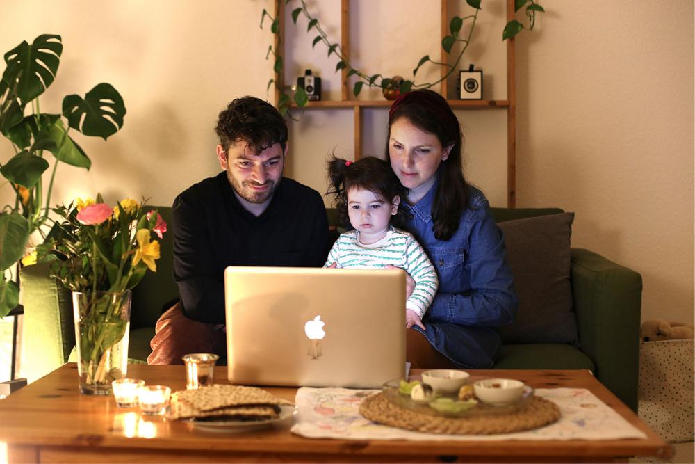 Ein Mann, ein Kind und eine Frau sitzen vor einem Laptop
