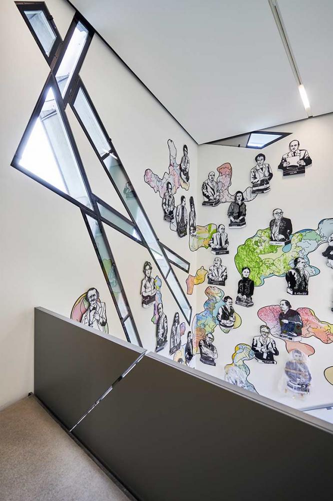 Blick von einer Treppe auf einer Wand mit comicartig gezeichneten Büsten berühmter Persönlichkeiten