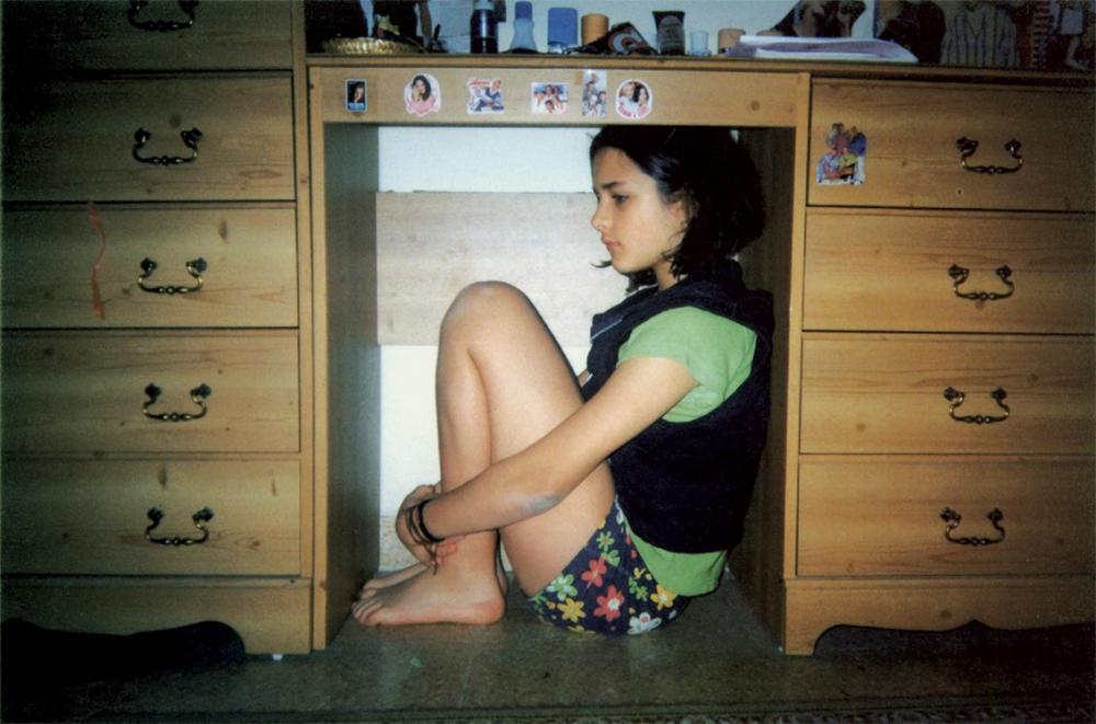 Ein Mädchen in kurzen Hosen kauert unter einem Schreibtisch