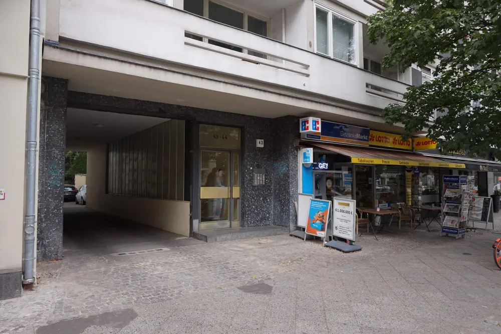 Color photo: Ground floor of a postwar building showing passageway, front door, and convenient store
