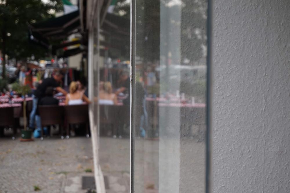 Color photo: View along a storefront showing people at a restaurant in the background