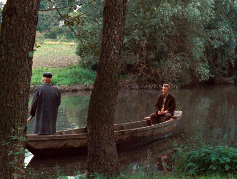 In einer üppig-grünen Landschaft fahren zwei Männer in einem Stocherkahn einen Fluss entlang. Einer der Männer sitzt, der andere stochert stehend.