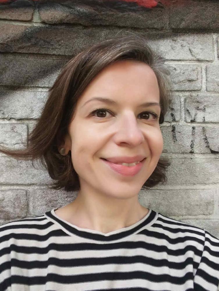 Selfie of Monika Flores in front of a brick wall sprayed with graffiti.