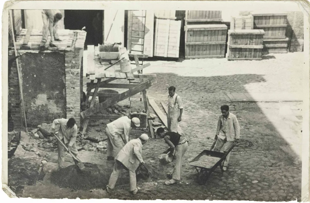 Seven men in working clothes and with wheelbarrow, shovels and other equipment (black and white photo).