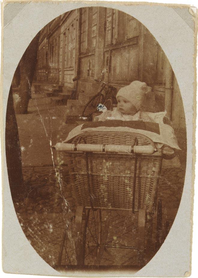Die hochformatige, oval vignettierte Aufnahme zeigt einen Säugling (Walter Frankenstein) im Kinderwagen aus geflochtenem Korb