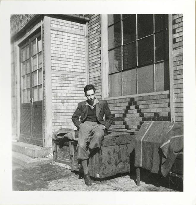 A young man sits in front of a house (black and white photo)