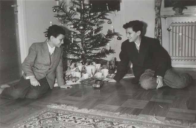 In the black-and-white photo, the two boys are sitting in front of a Christmas tree, smiling at the gifts that are strewn beneath it.