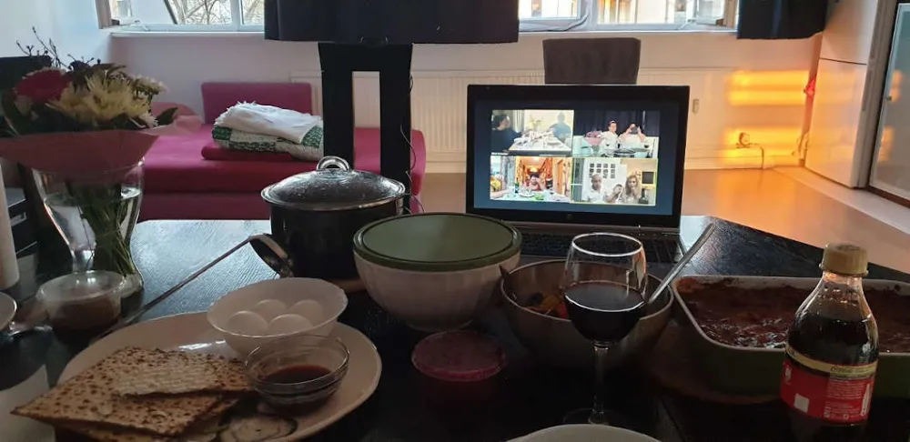 On a table, behind the food, there is a laptop in which a video chat is open.