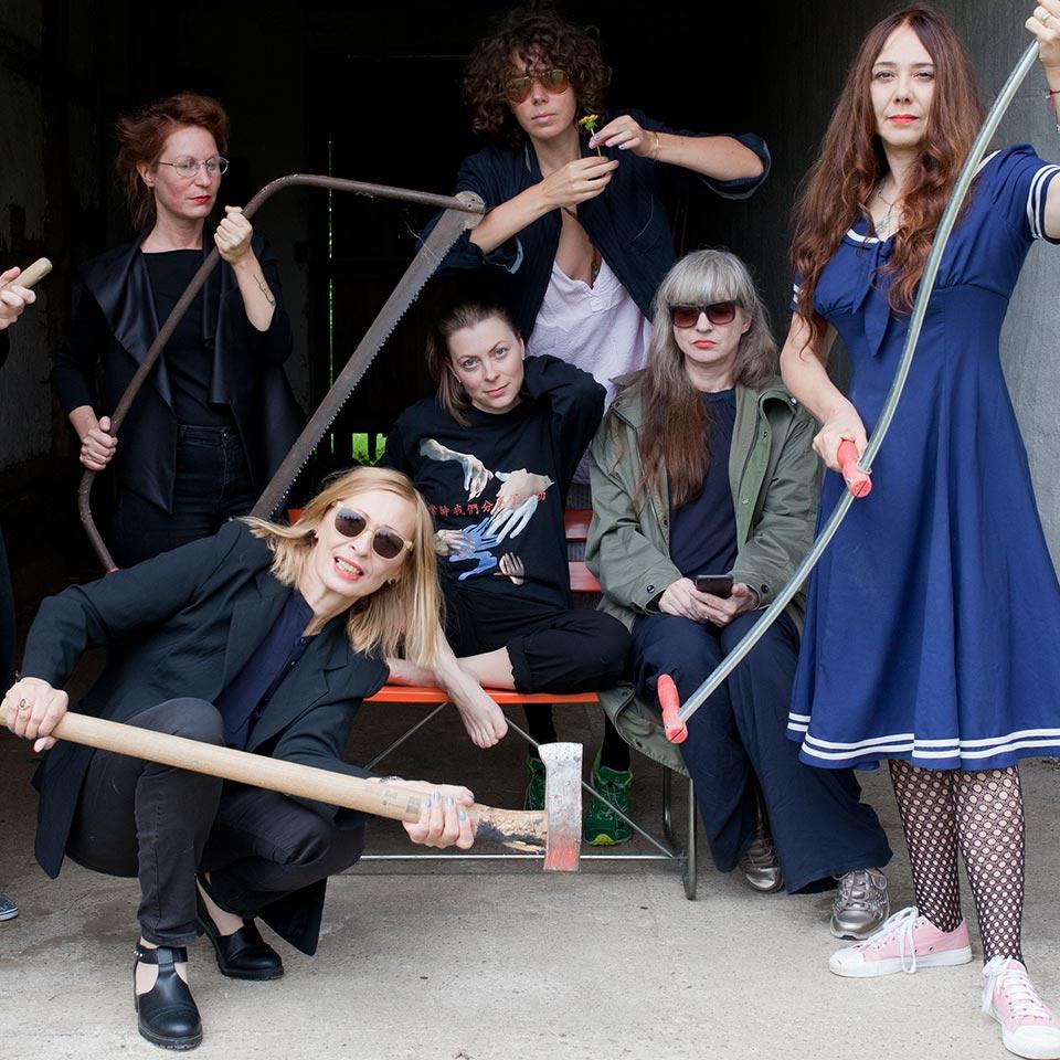 Group photo of the musicians from “Monika Werkstatt”. Some of the woman present each one of the following objects: an axe, a sickle, a saw and a flower.