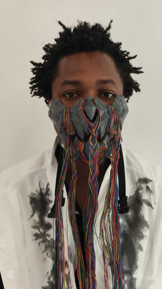 Portr&auml;t eines Mannes mit ungew&ouml;hnlicher Maske vor Mund und Nase aus grauem Plastik und vielen bunten Schn&uuml;ren.