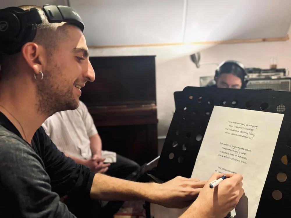 Ein junger Man mit Ohrring notiert mit einem Stift etwas auf einem Textblatt, das auf einem Notenst&auml;nder steht.
